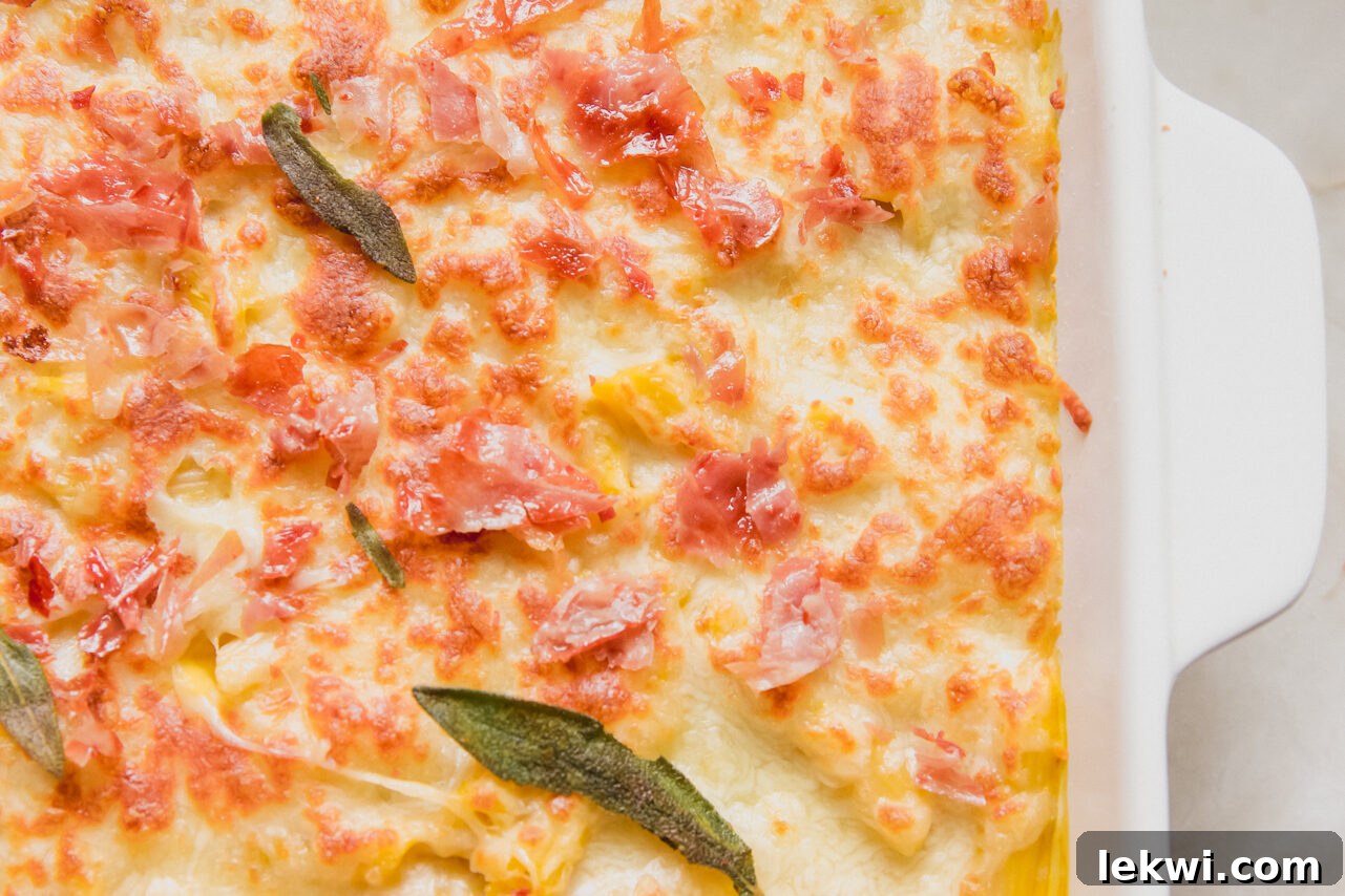 Finished butternut pasta bake, golden and bubbly from the broiler, adorned with crispy sage leaves and chopped prosciutto, served in a rustic baking dish.