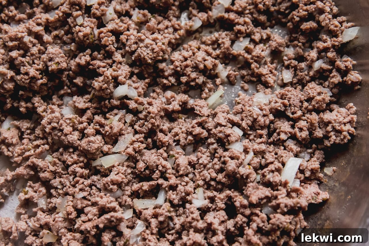 Ground beef and diced onion browning in a large pan on the stovetop.