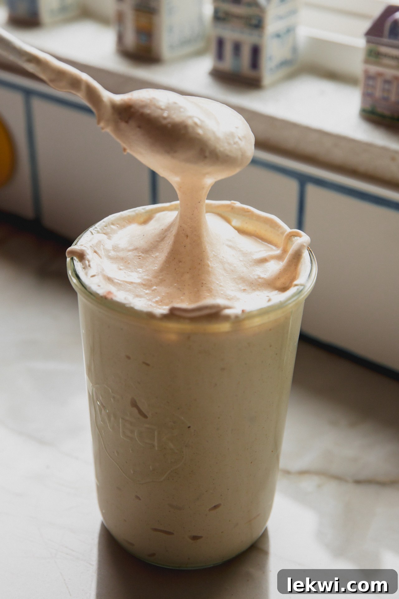 A spoon putting pumpkin pie marshmallow fluff into a glass jar.