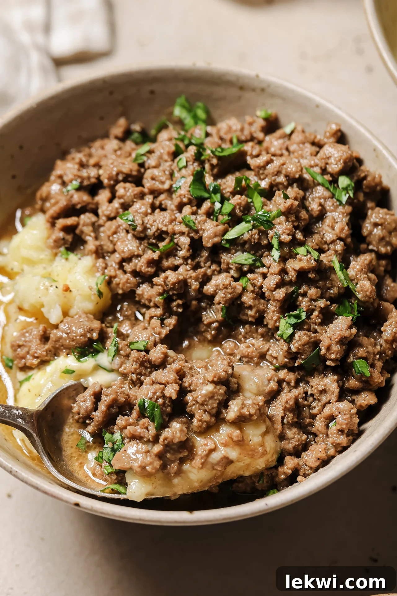 Hearty Ground Beef and Gravy served over a bed of creamy mashed potatoes in a cozy bowl, garnished with fresh parsley.