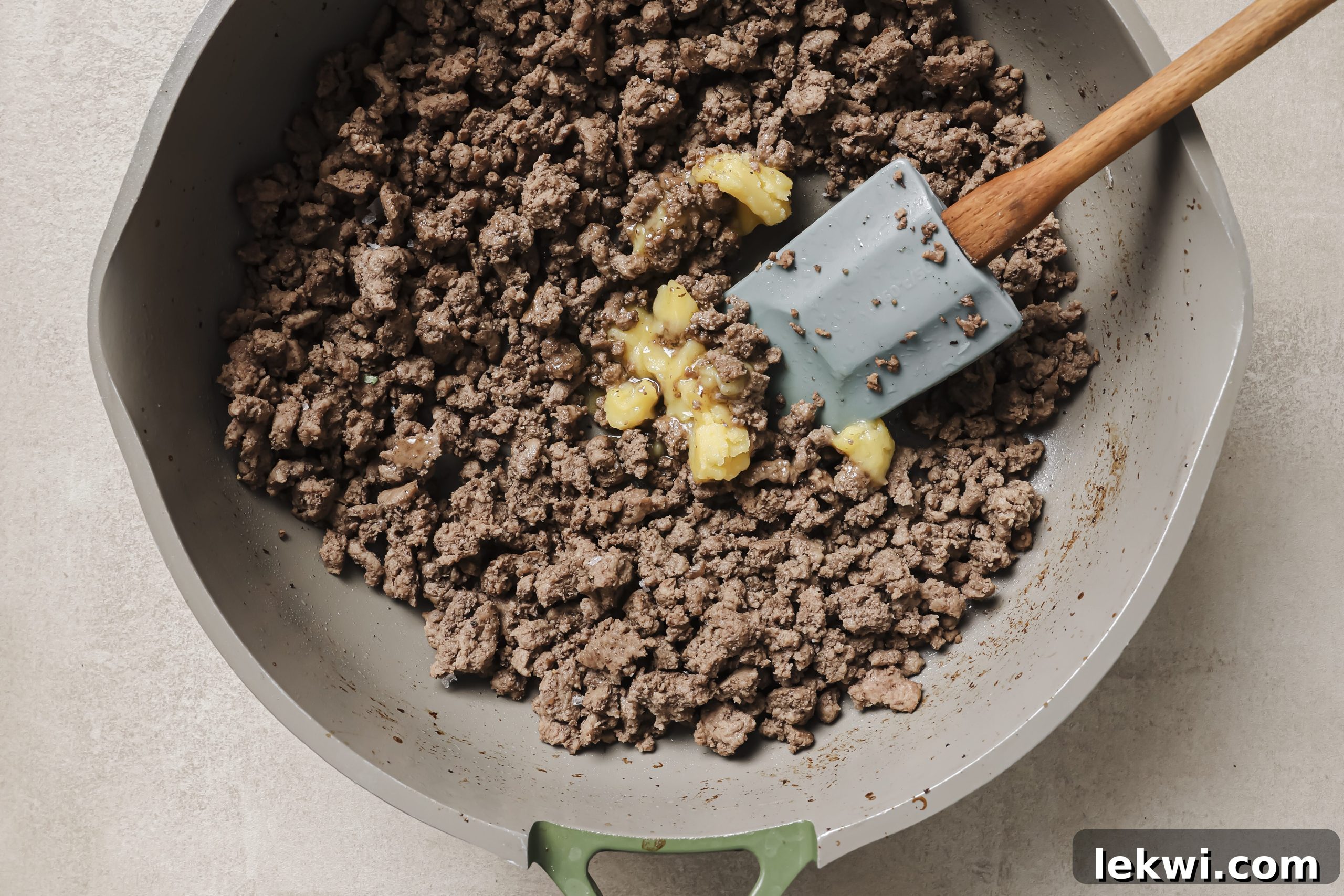 Melted ghee added to the browned ground beef in the pan, ready for aromatics.