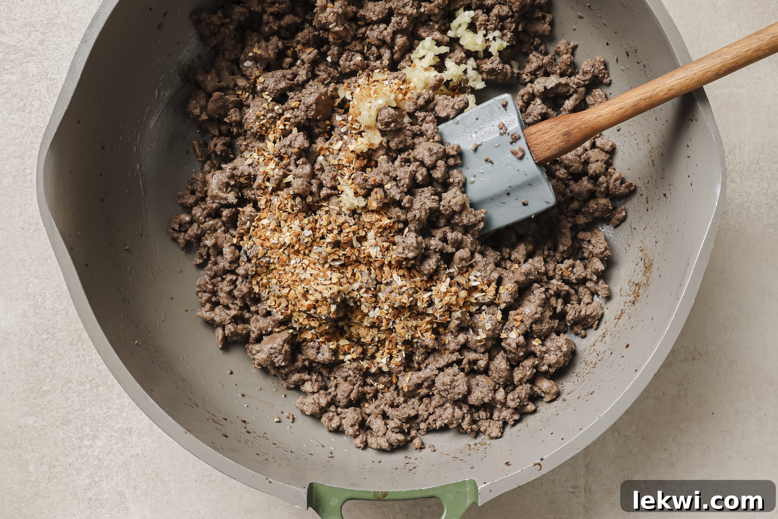 Sautéing minced garlic and dried minced onion with browned ground beef in a pan.