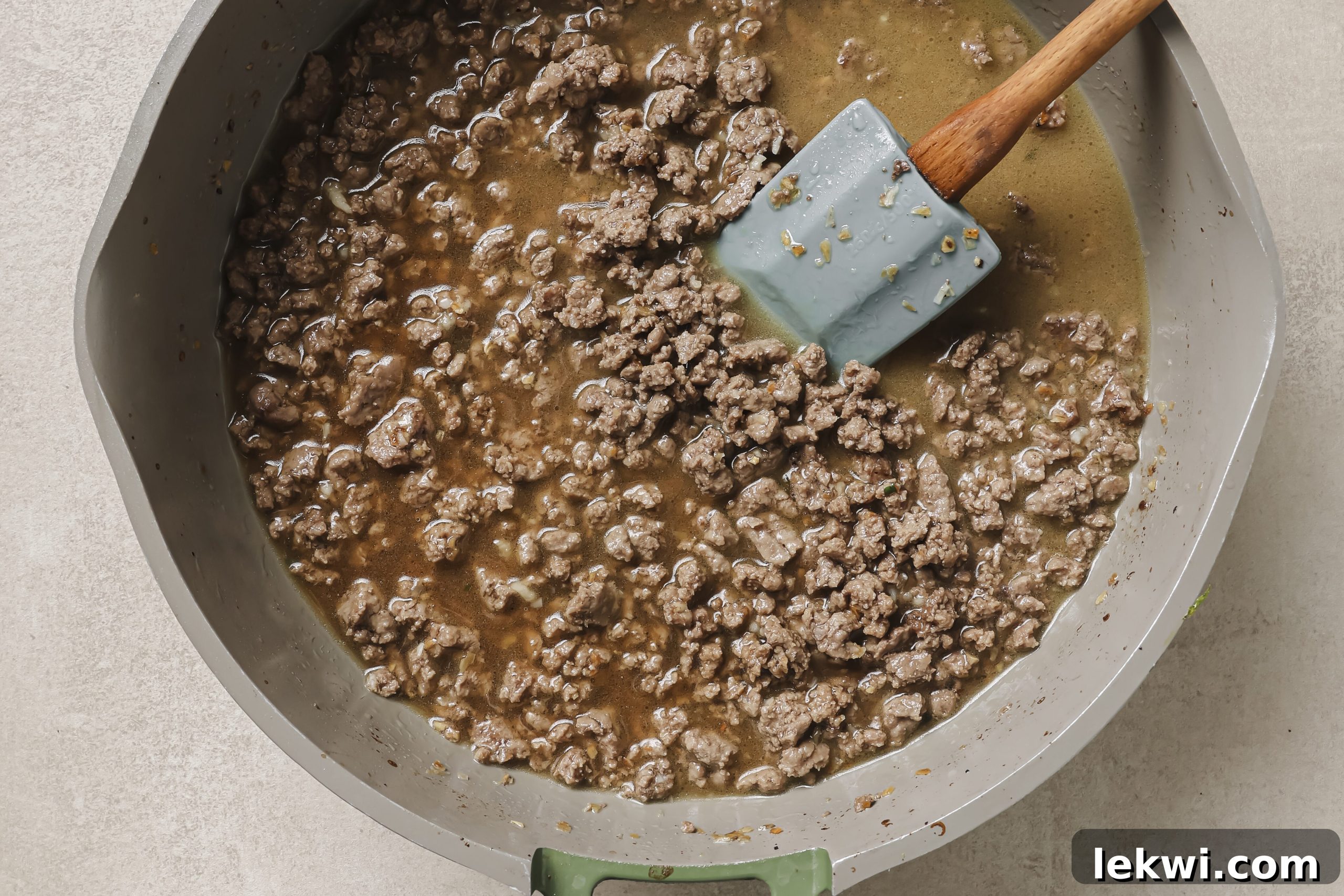Pouring beef broth into the pan with ground beef and starch, stirring constantly to combine.
