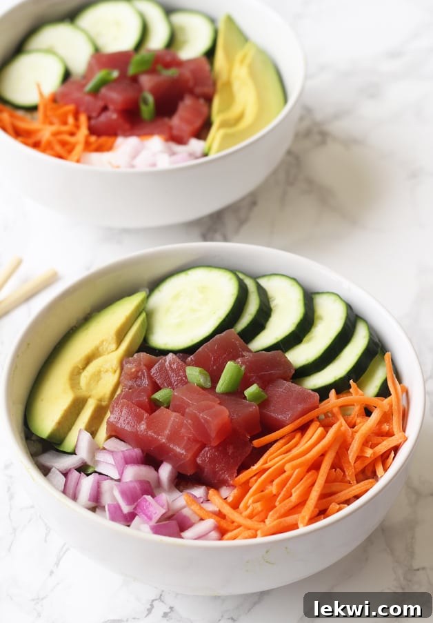 A vibrant bowl featuring fresh tuna poke, crisp cucumbers, creamy avocado slices, finely diced red onions, and shredded carrots, all artfully arranged for a delicious and healthy meal.