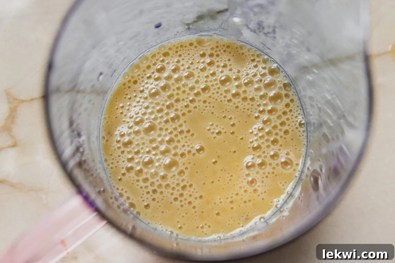 The wet ingredients, including mashed banana, egg, egg whites, vanilla, and maple syrup, are blended together until smooth in a tall container.