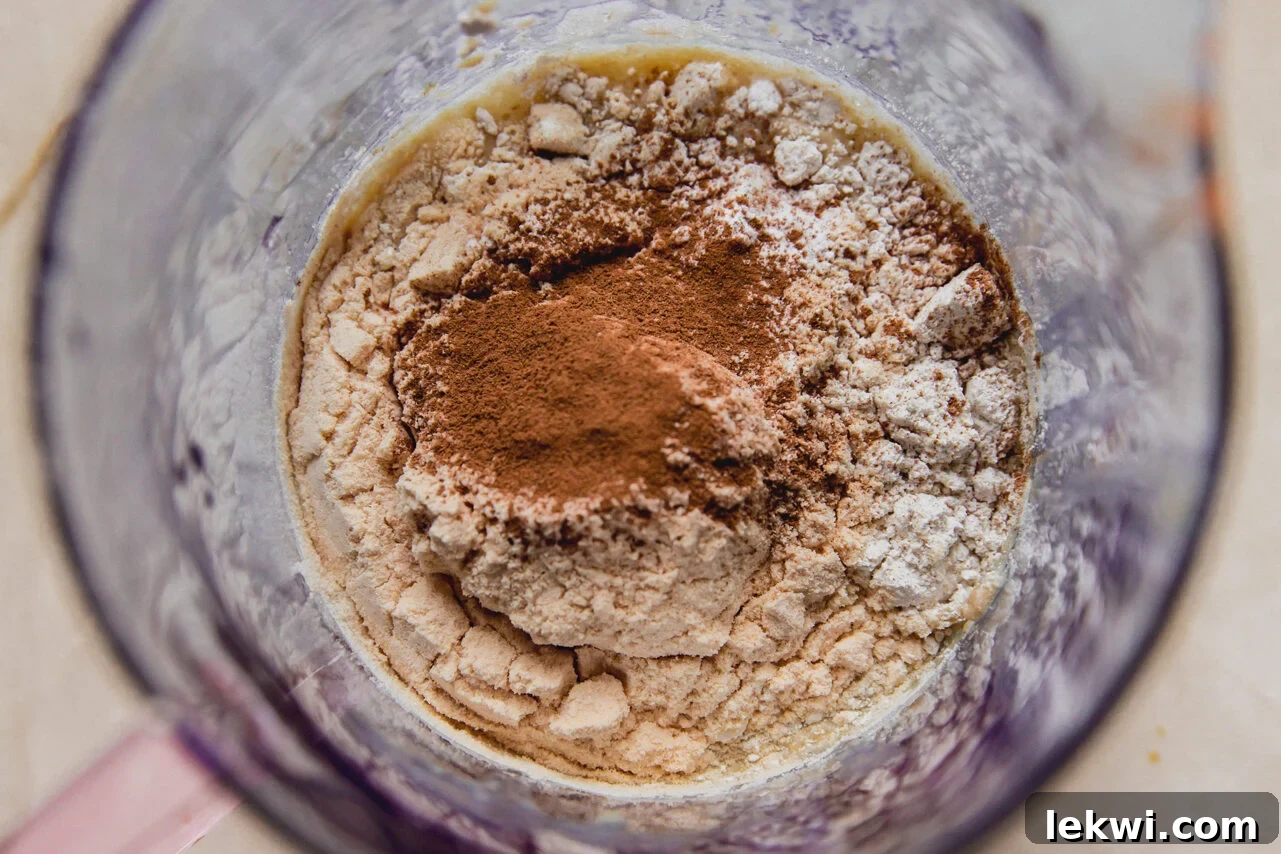 The dry ingredients – protein powder, baking powder, oat flour, and cinnamon – are added to the blended wet ingredients before the final blend.