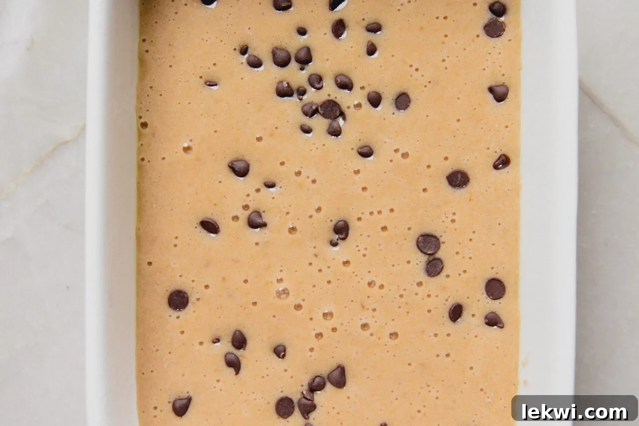 The smooth banana protein cake batter is poured into a prepared baking dish, with mini chocolate chips sprinkled on top.