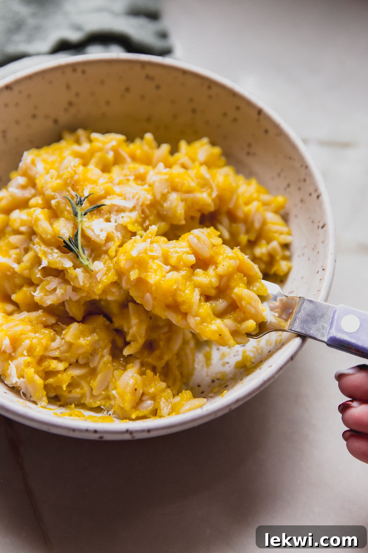 A close-up shot of a spoon scooping a generous portion of creamy pumpkin orzo from a serving bowl, showcasing its rich texture.
