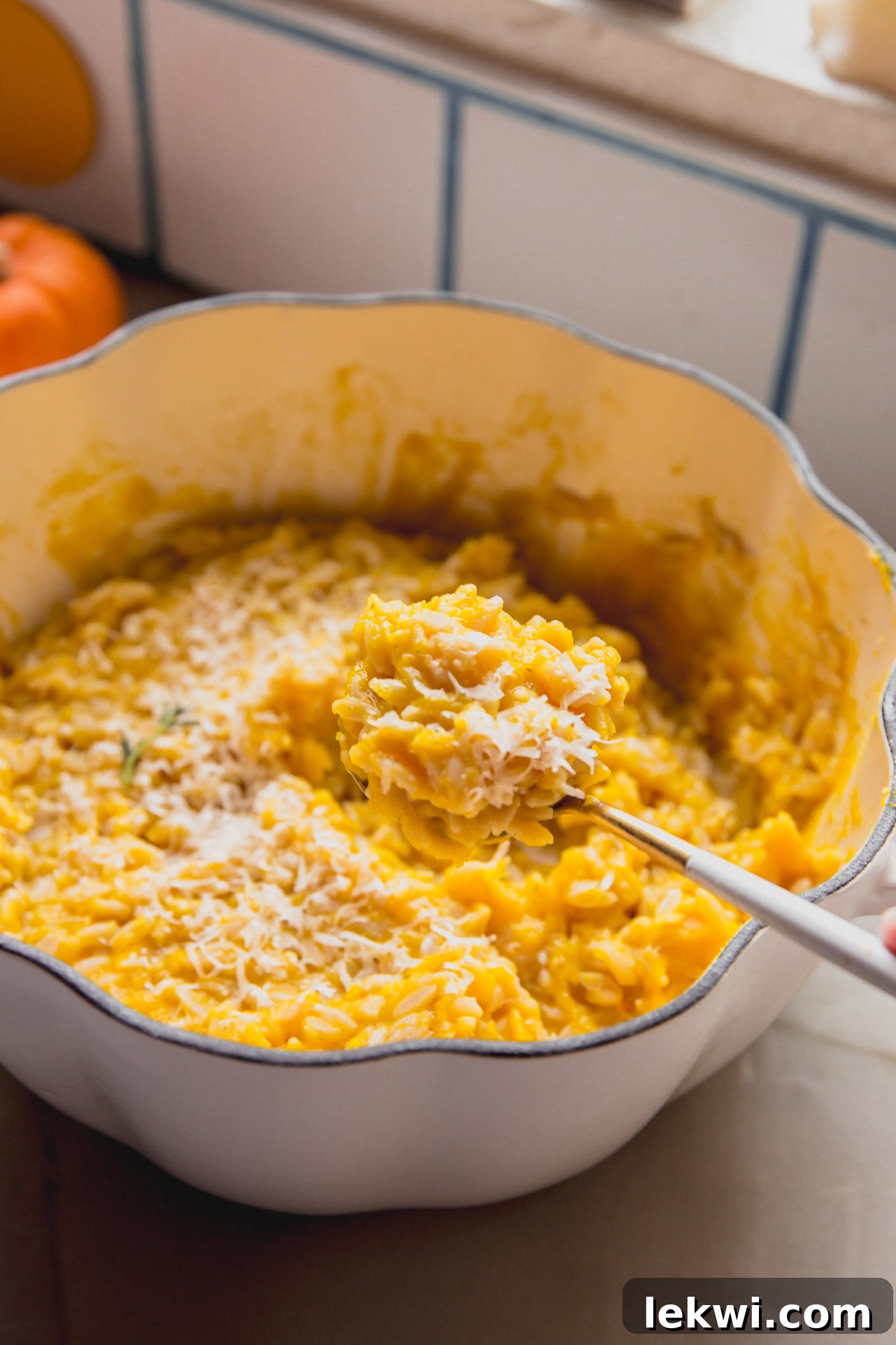 A serving spoon taking a portion of pumpkin orzo from a large, rustic serving dish, ready for sharing.