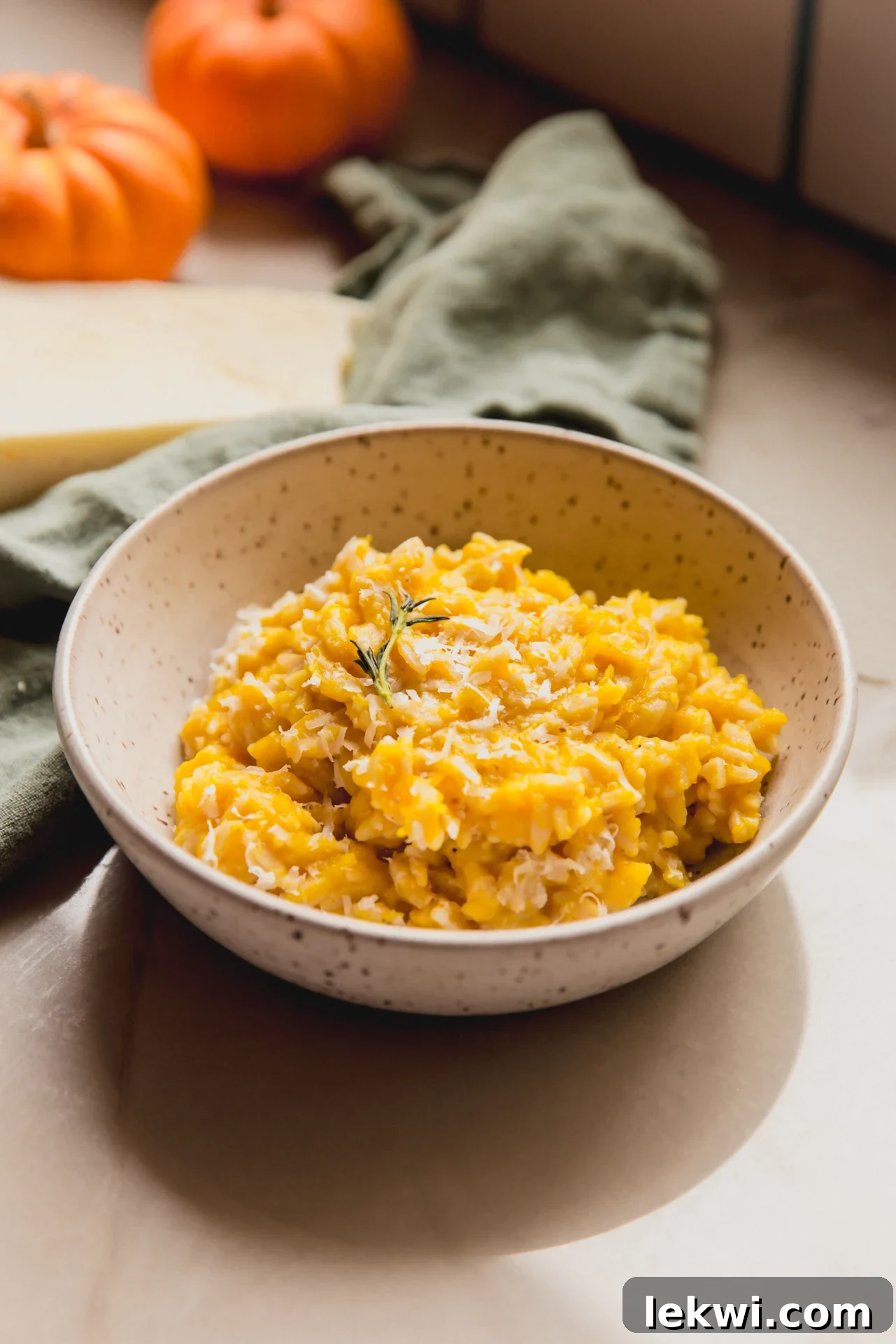 A bowl of creamy pumpkin orzo, garnished with fresh thyme, emphasizing its vibrant color and inviting texture.