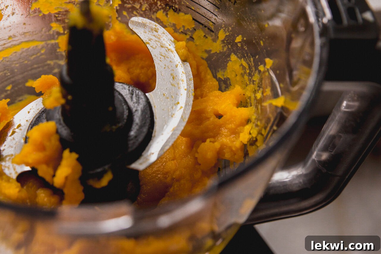 The soft, roasted pumpkin flesh being spooned into a food processor for puréeing.