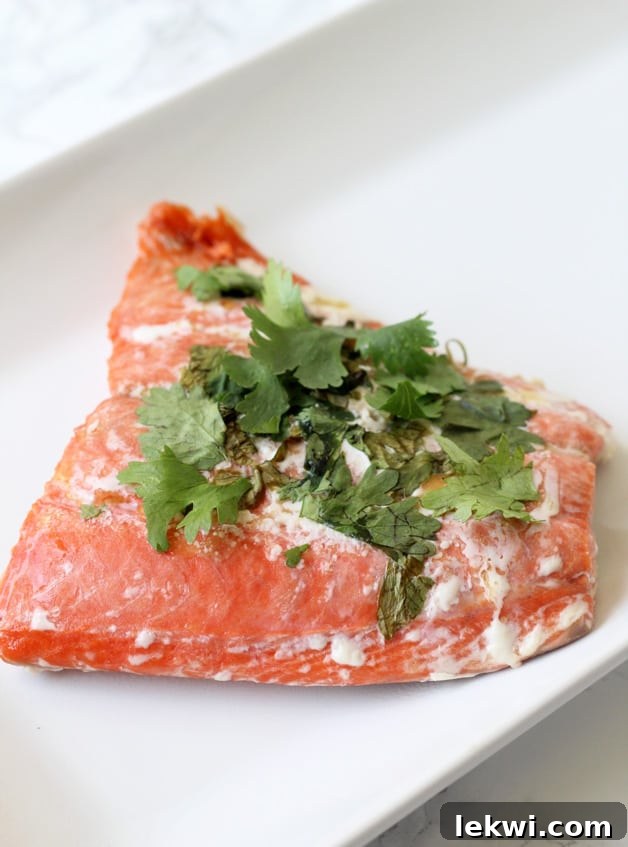 A piece of salmon topped with cilantro after cooking sitting on a white plate.