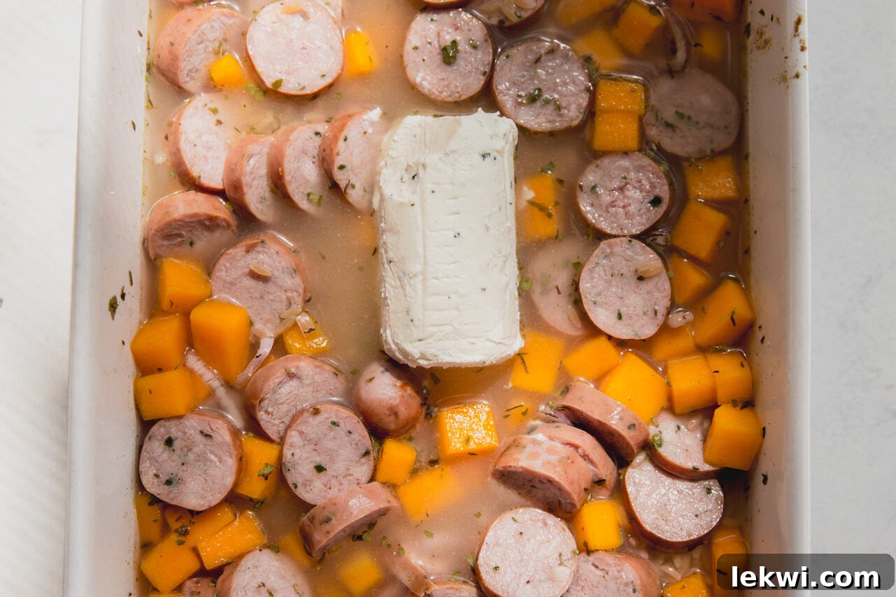 The ingredients for chicken sausage and orzo being added to the baking dish with the pre-cooked squash.