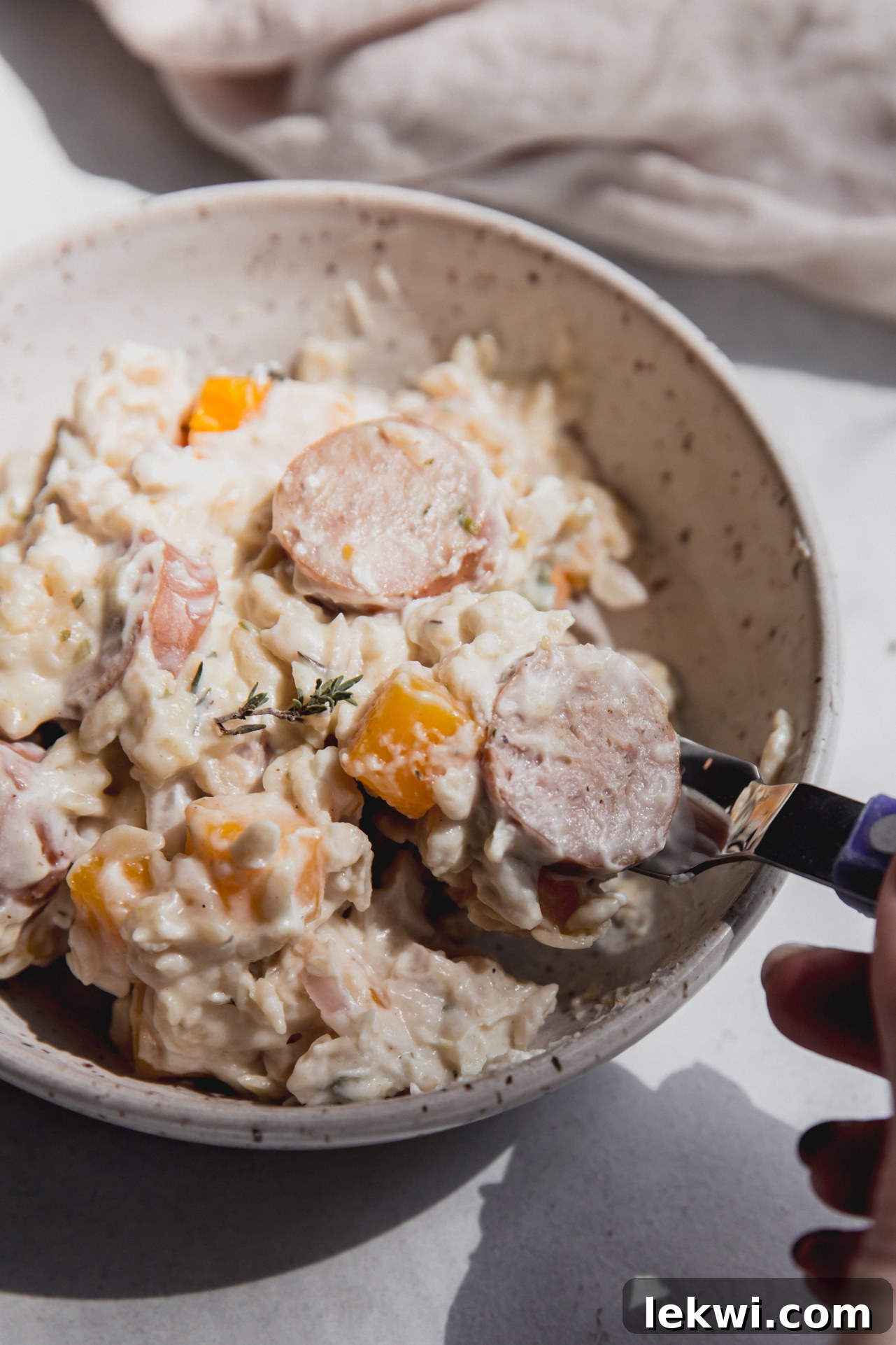 A bowl of creamy chicken sausage and orzo bake with a spoon taking a bite.