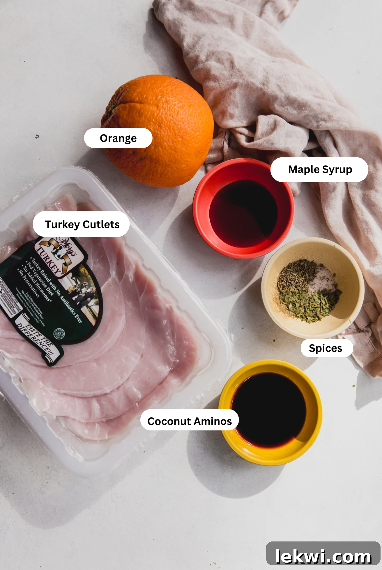 A flat lay of all the fresh ingredients including turkey cutlets, oranges, herbs, and oils, laid out on a kitchen counter.