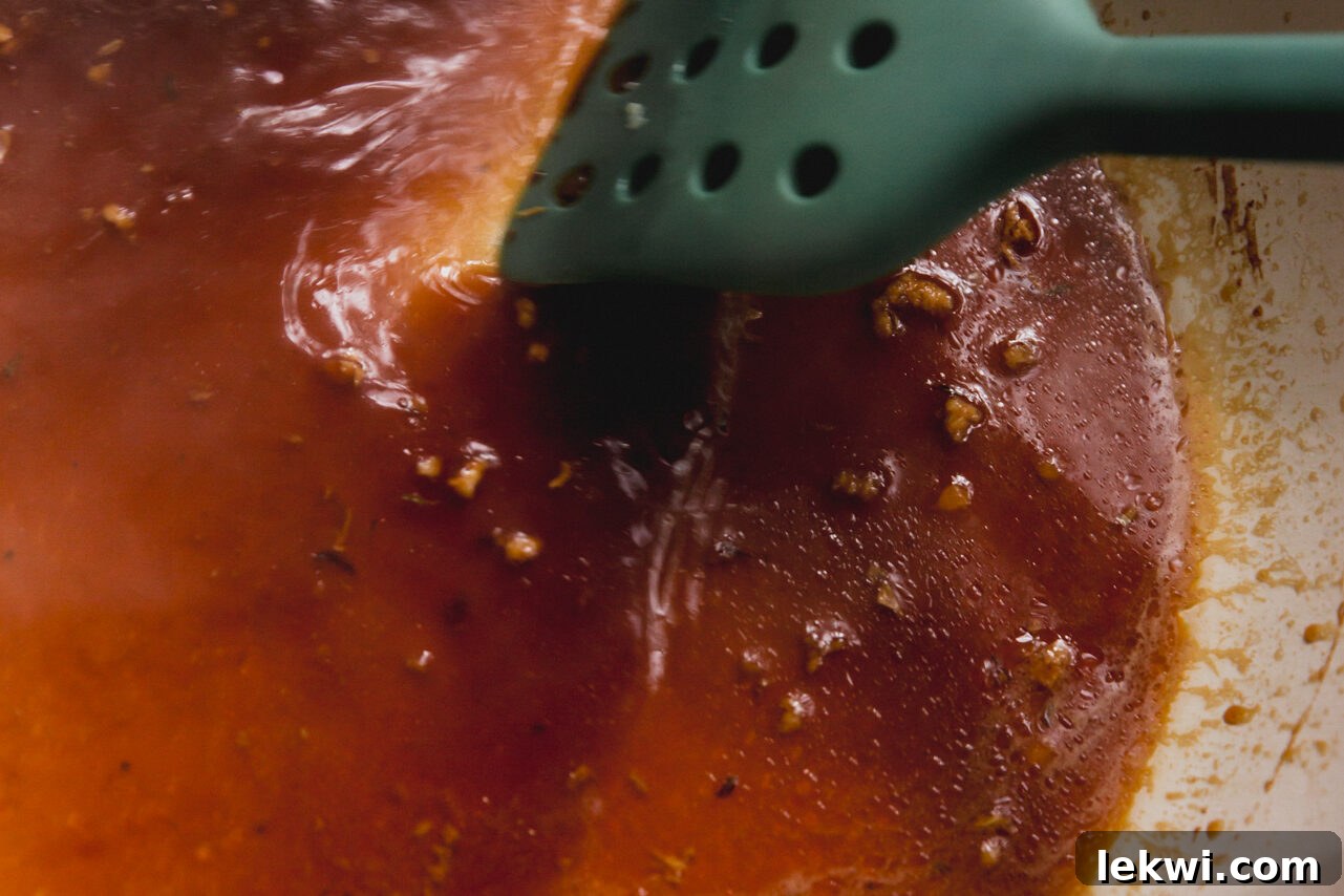 A pan with cooking residue being deglazed with coconut aminos, showing the liquid being stirred.