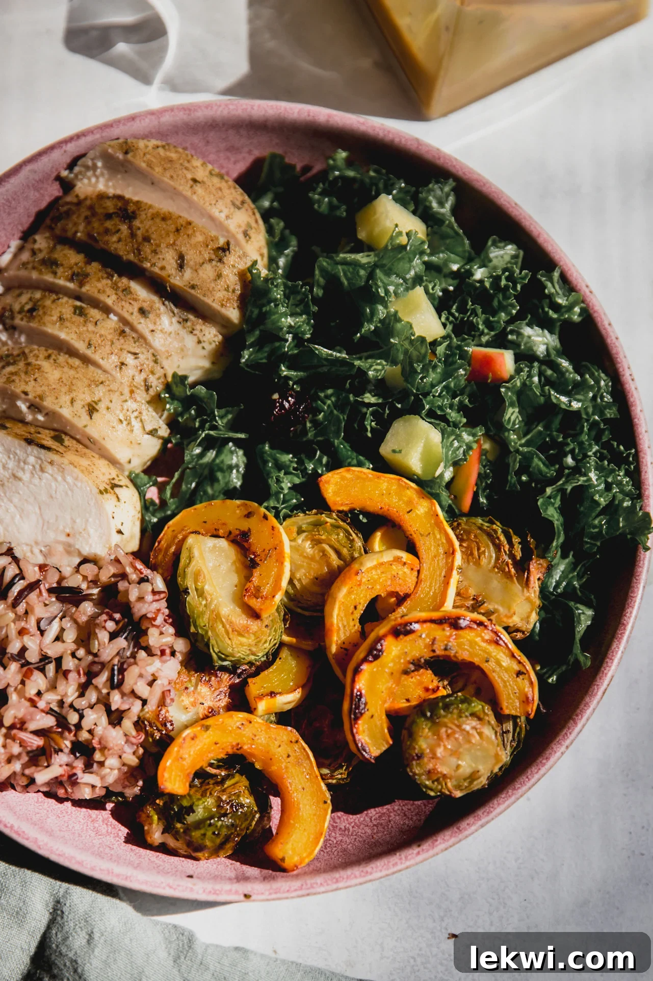A beautifully presented roasted delicata squash, kale salad, wild rice, and chicken in a vibrant pink bowl, ready for a delicious fall meal.