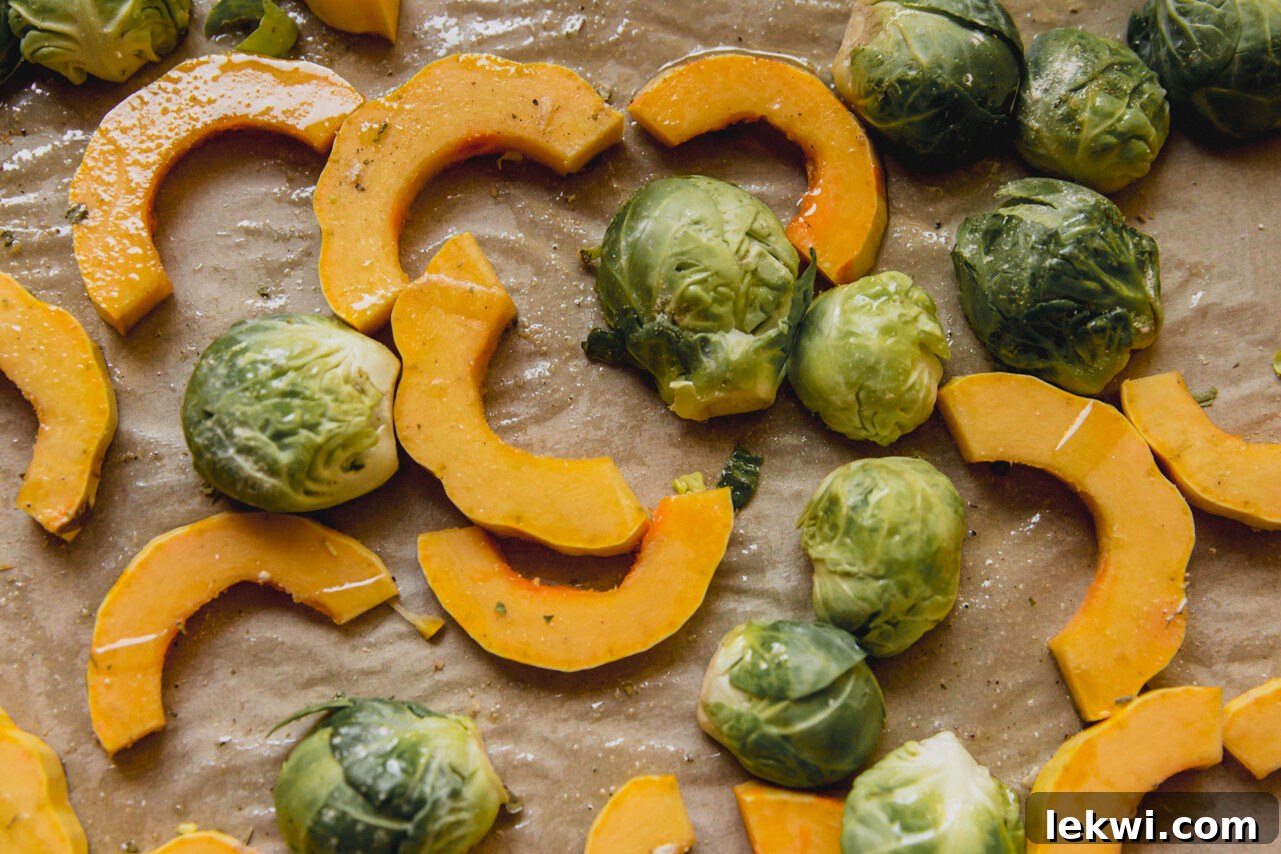 Delicata squash half-moons and halved brussels sprouts seasoned with herbs and oil on a baking sheet, ready for roasting.