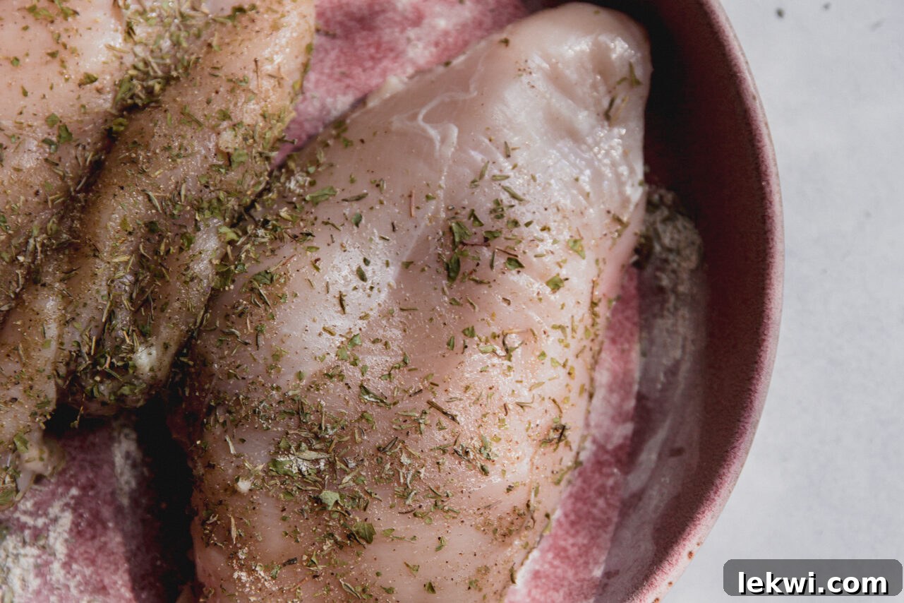Raw chicken breast seasoned with various herbs and spices in a mixing bowl, ready for cooking.