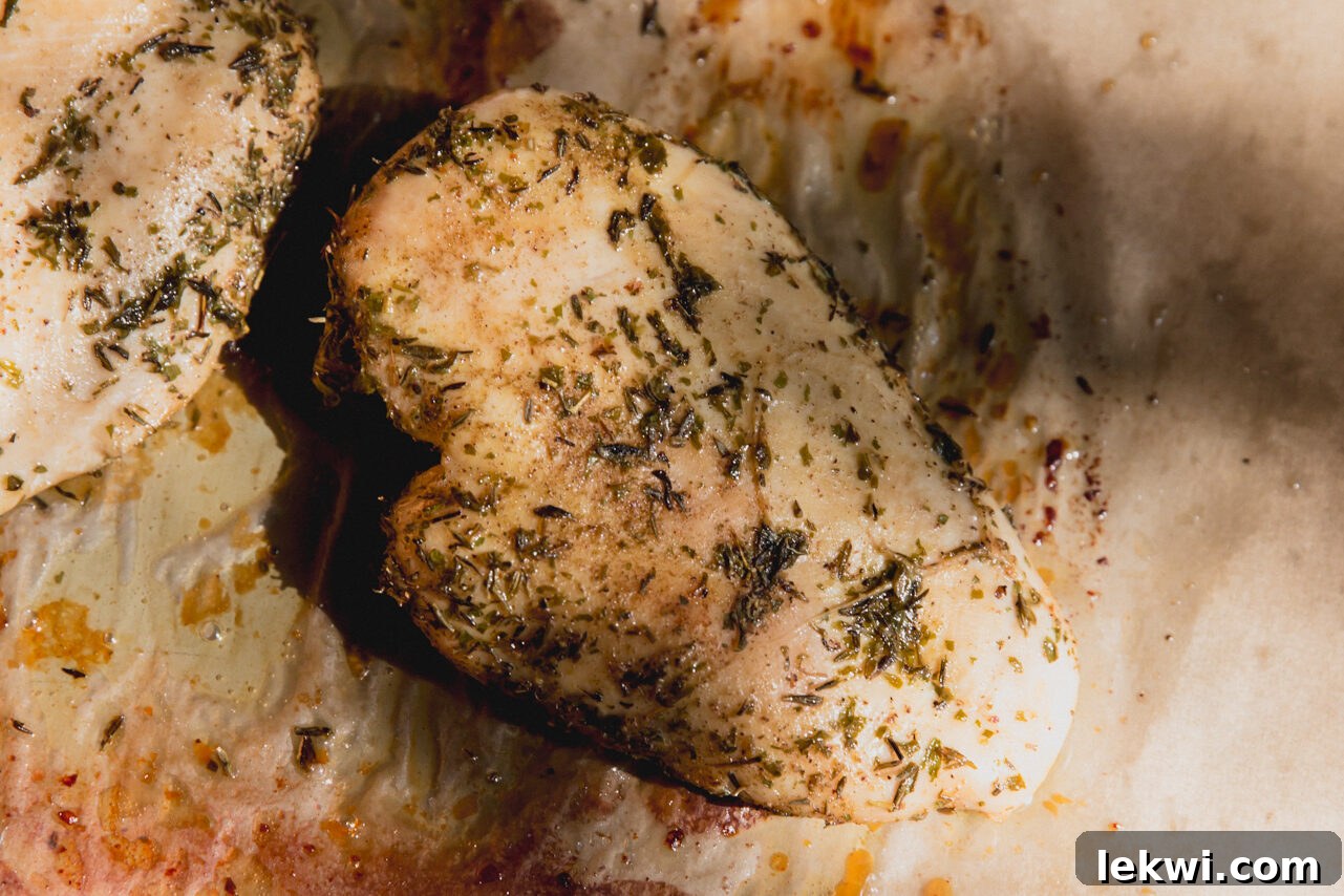 Cooked, golden-brown chicken breast resting on a sheet pan after being roasted, ready for slicing.
