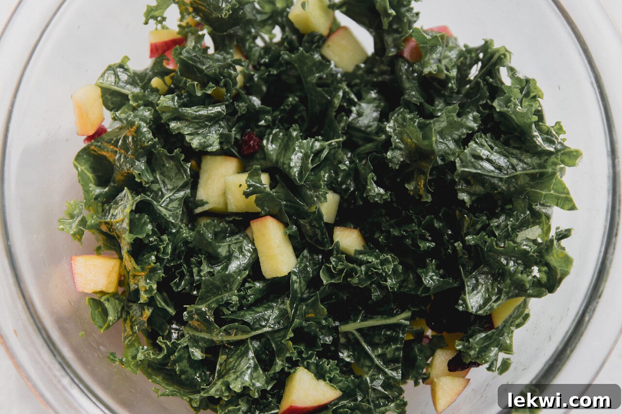 A vibrant kale salad with diced apples and dried cranberries in a large mixing bowl.