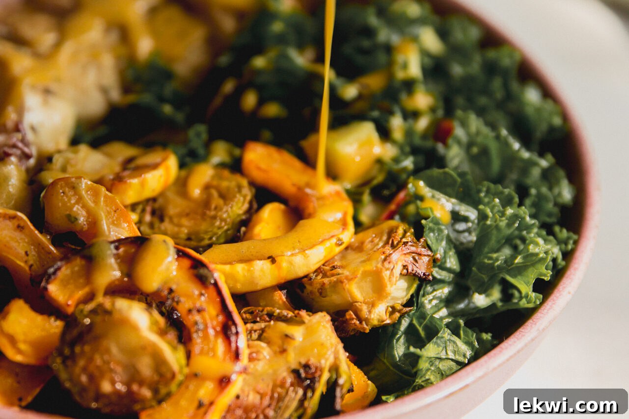A finished harvest chicken bowl with roasted squash, wild rice, kale salad, and sliced chicken, being drizzled with a rich maple Dijon dressing.