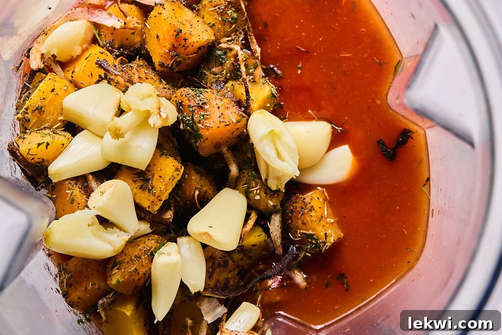 Roasted butternut squash, garlic, shallot, pasta sauce, and broth in a blender, ready to be pureed into a smooth sauce.