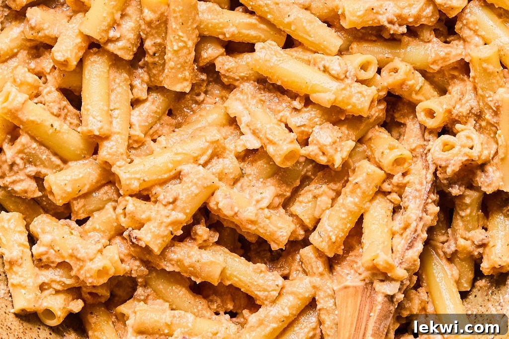 Al dente cooked pasta noodles gently coated in the creamy cheese mixture within a large mixing bowl.