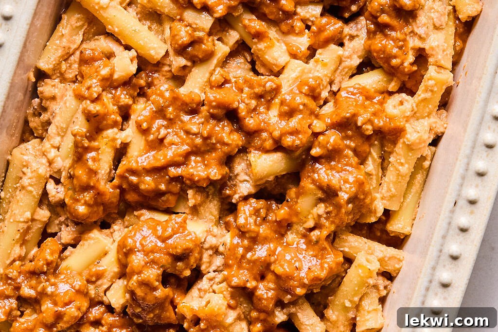 Layers of cheese-coated pasta and butternut squash meat sauce alternating in a casserole dish before baking.