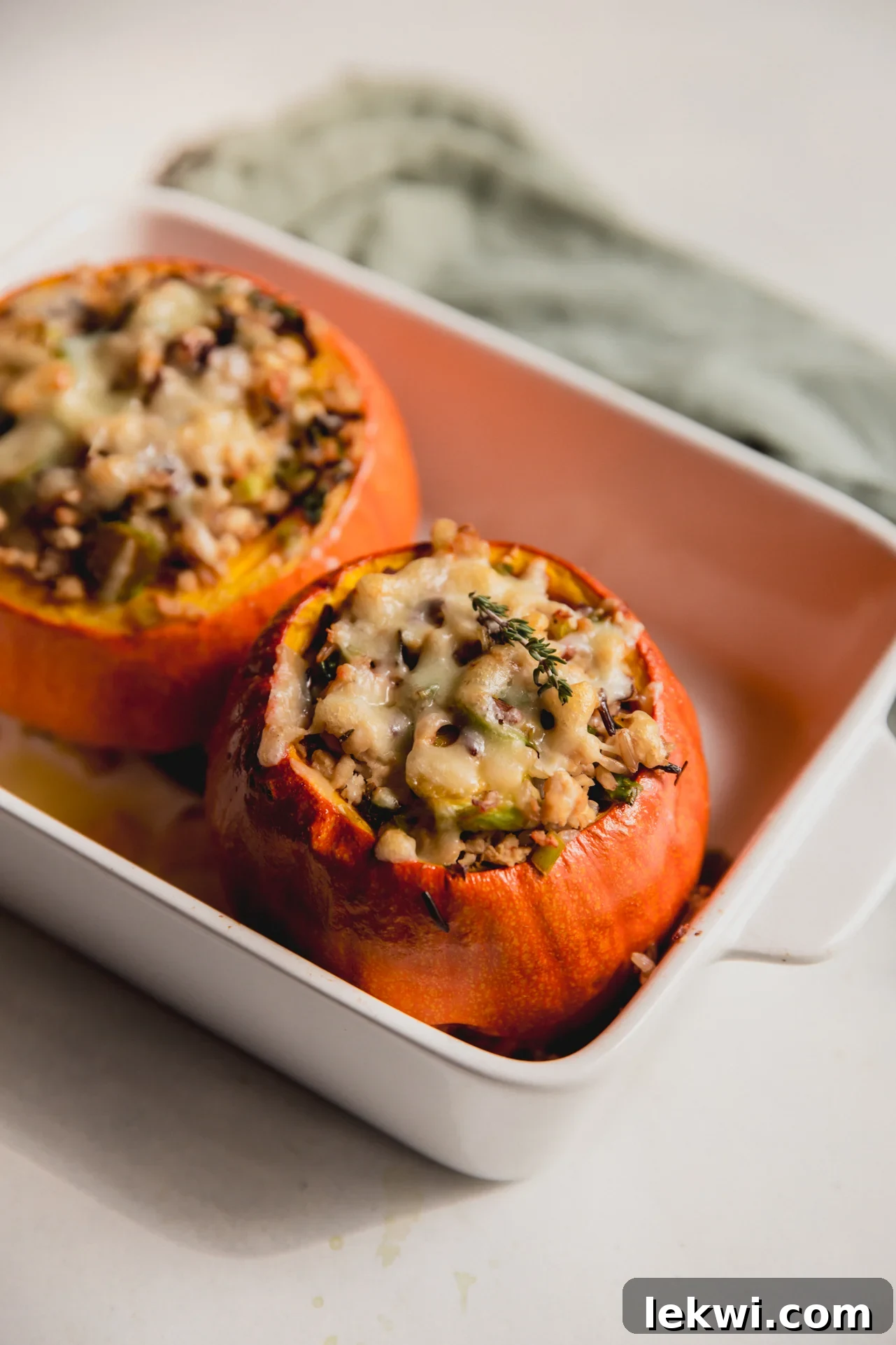 Two roasted stuffed pumpkins in a baking dish, brimming with savory wild rice and turkey filling.