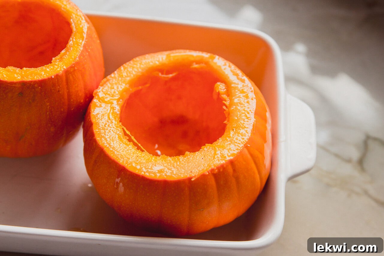 Uncooked pumpkins with their tops removed and insides scooped clean, ready for roasting in a baking dish.