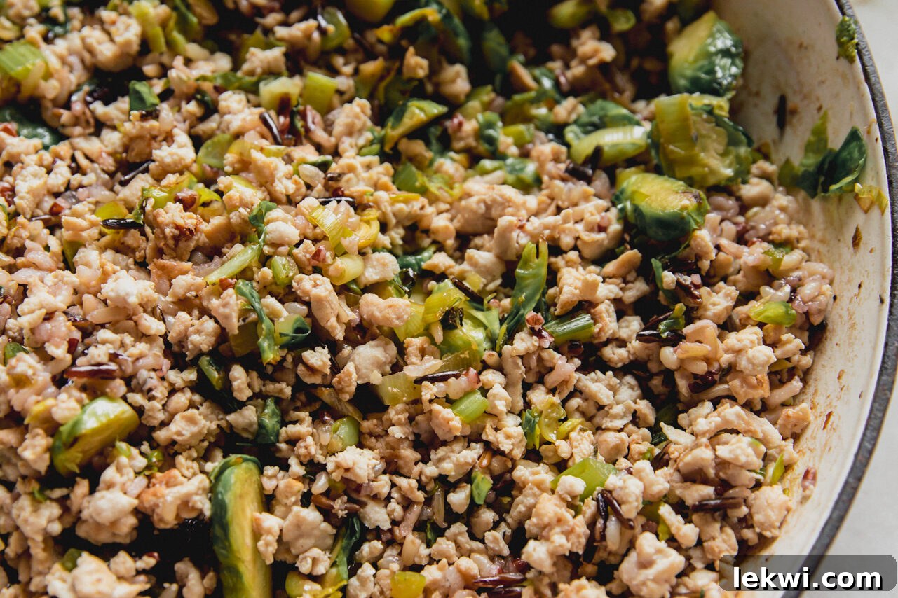 A pan filled with cooked ground turkey, shredded Brussels sprouts, wild rice, and dried cranberries, forming the savory stuffing.