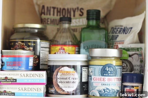 A shot of a pantry filled with coconut cream, ghee, sardines, olive oil, and apple cider vinegar among other things, demonstrating a well-stocked Paleo AIP kitchen.