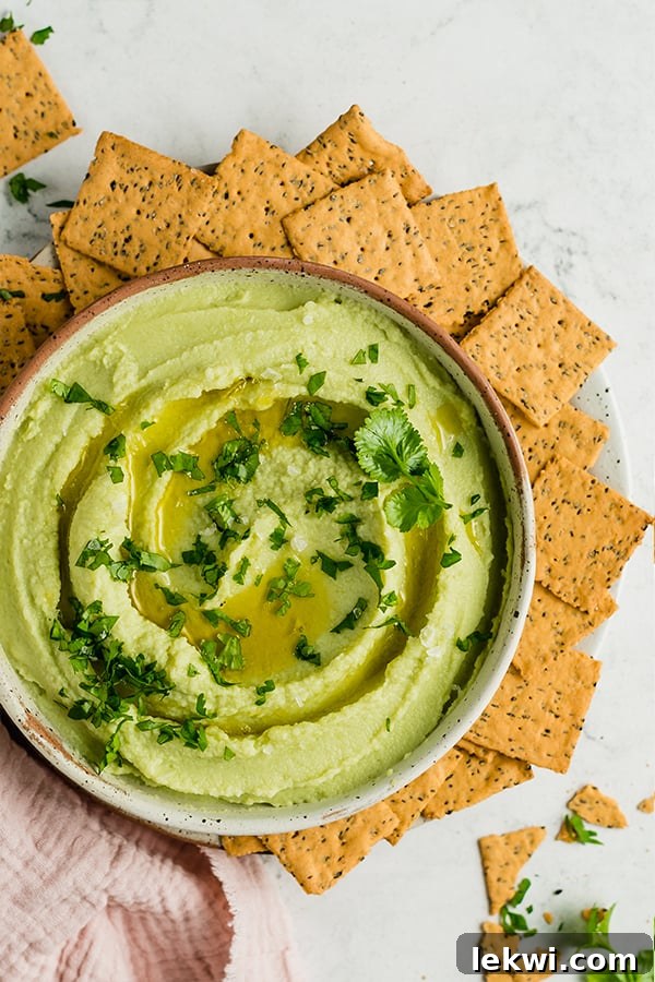 Crackers around a bowl of avocado cauliflower hummus, a perfect healthy dip.
