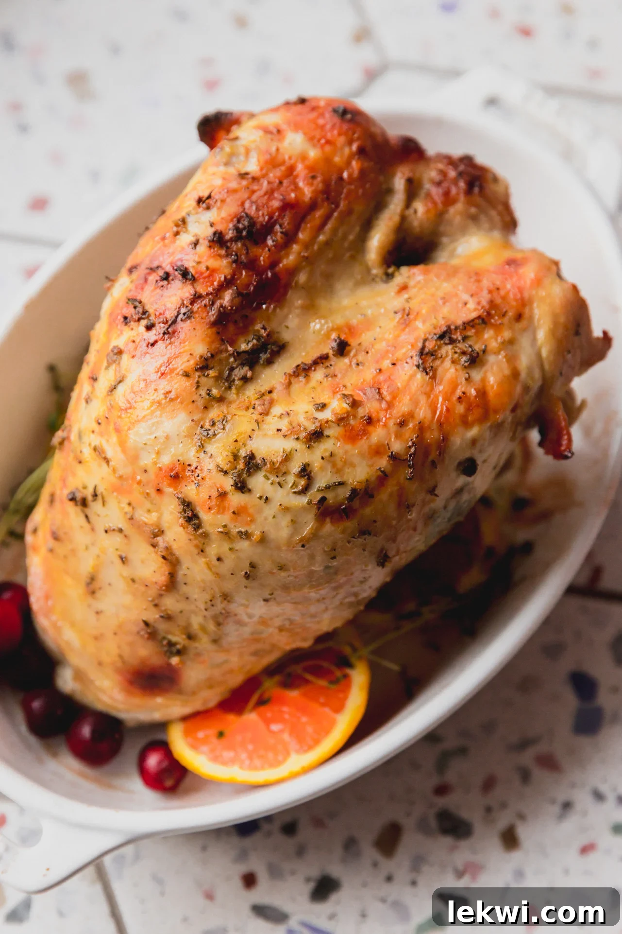 Fully cooked slow cooker turkey breast with crispy skin in a white serving dish, garnished with fresh herbs and orange slices.