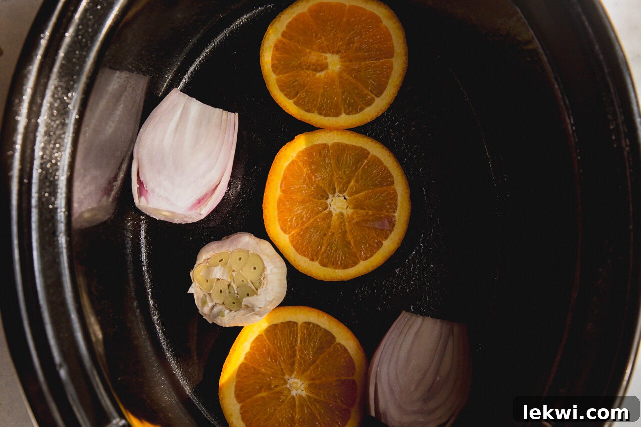 The slow cooker with a base of orange slices, whole garlic head, and halved shallots ready for the turkey.