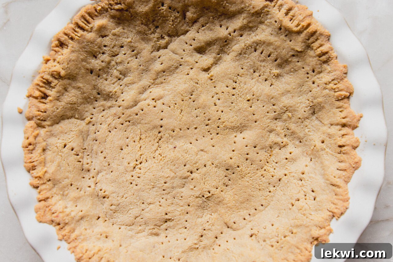 A freshly baked, golden-brown almond flour pie crust carefully pressed into a 9-inch pie pan, with fork marks visible for venting.
