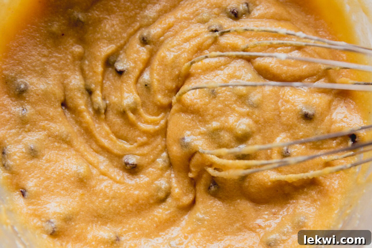 A smooth, light-colored chocolate chip cookie pie filling being vigorously whisked in a clear glass bowl, showcasing its creamy consistency.