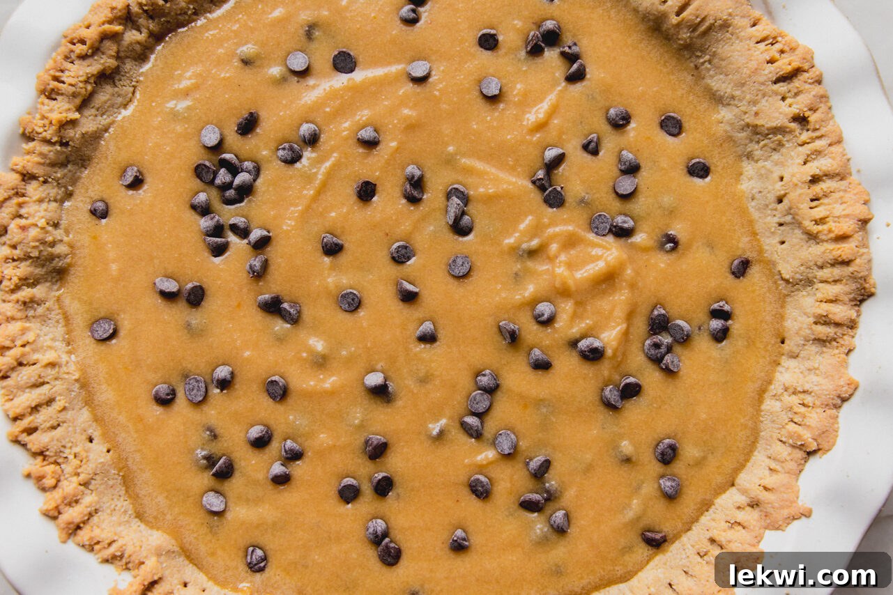 The unbaked chocolate chip cookie pie filling, studded with chocolate chips, carefully poured into the pre-baked almond flour crust within a large pie pan.