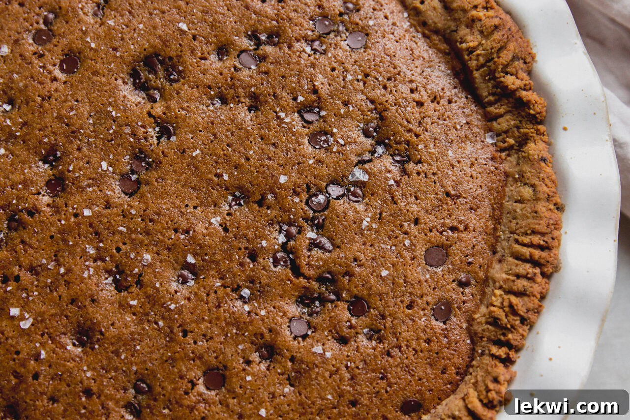A freshly baked gluten-free chocolate chip cookie pie in a large white pie pan, cooling on a wire rack after being removed from the oven, showing golden-brown edges and a set center.