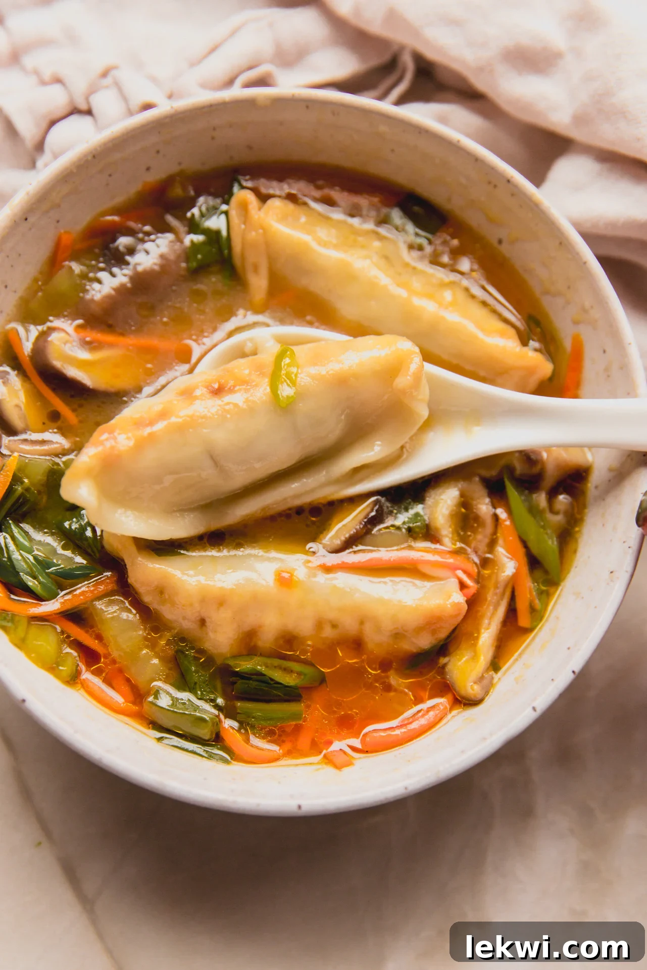 A steaming bowl of delicious gluten-free potsticker soup, garnished with green onions, with a spoon scooping a potsticker.
