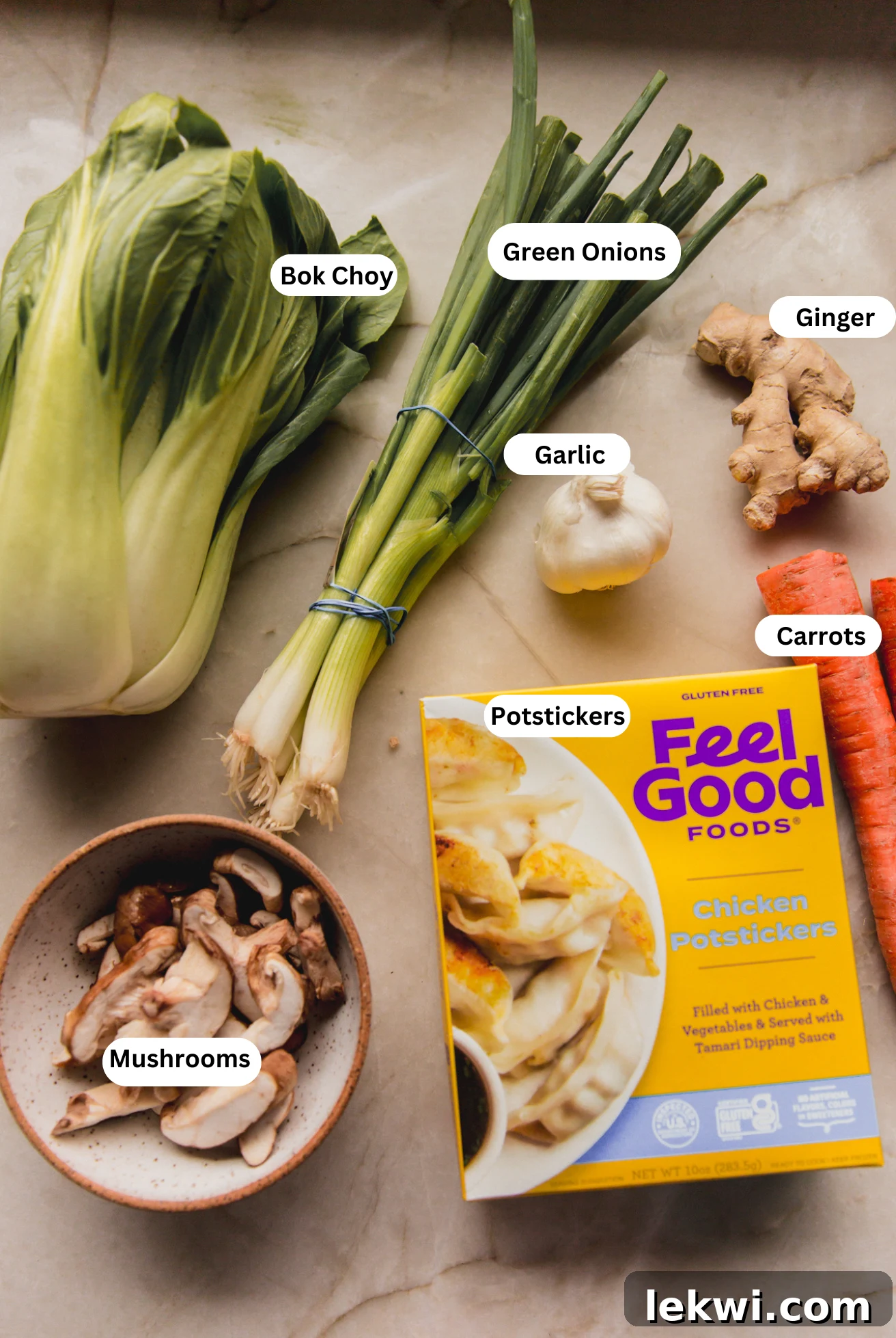 A collection of fresh ingredients laid out on a white surface, including bok choy, shiitake mushrooms, ginger, garlic, and gluten-free potstickers, ready for making soup.