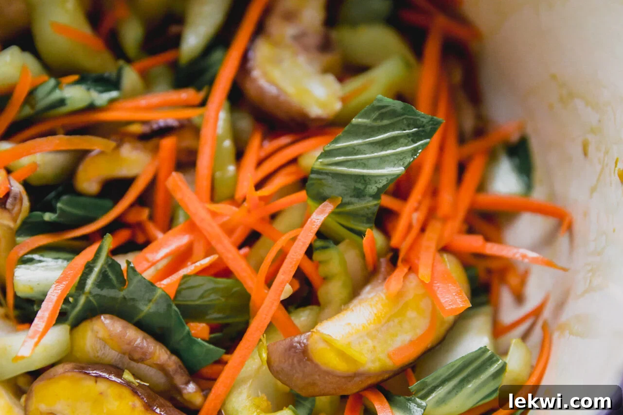 A close-up view of minced garlic, grated ginger, and sliced vegetables (shiitake mushrooms, bok choy, shredded carrots) gently sautéing in a hot pan.