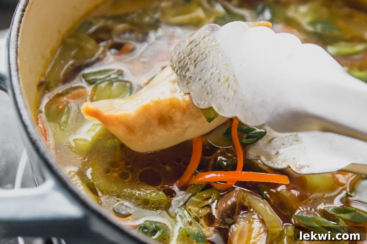 Metal tongs carefully placing cooked potstickers back into a simmering pot of broth and vegetables on the stove.
