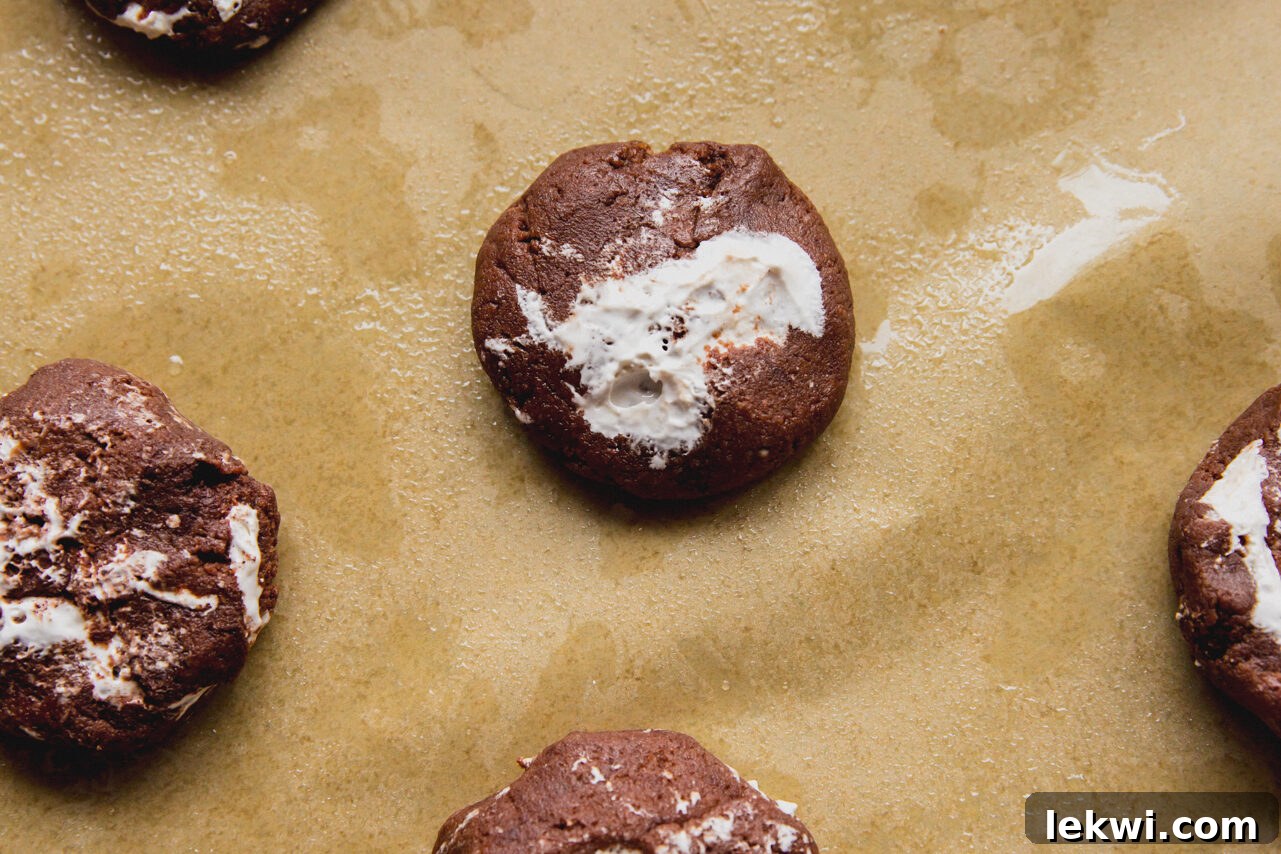 Six freshly baked chocolate marshmallow fluff cookies arranged on a piece of parchment paper, showing their perfectly rounded shape and slight golden edges.