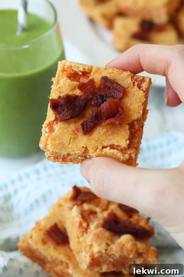 A hand holding a delicious sweet potato bacon bar, showcasing its moist texture and golden-brown crust, with flecks of bacon visible.