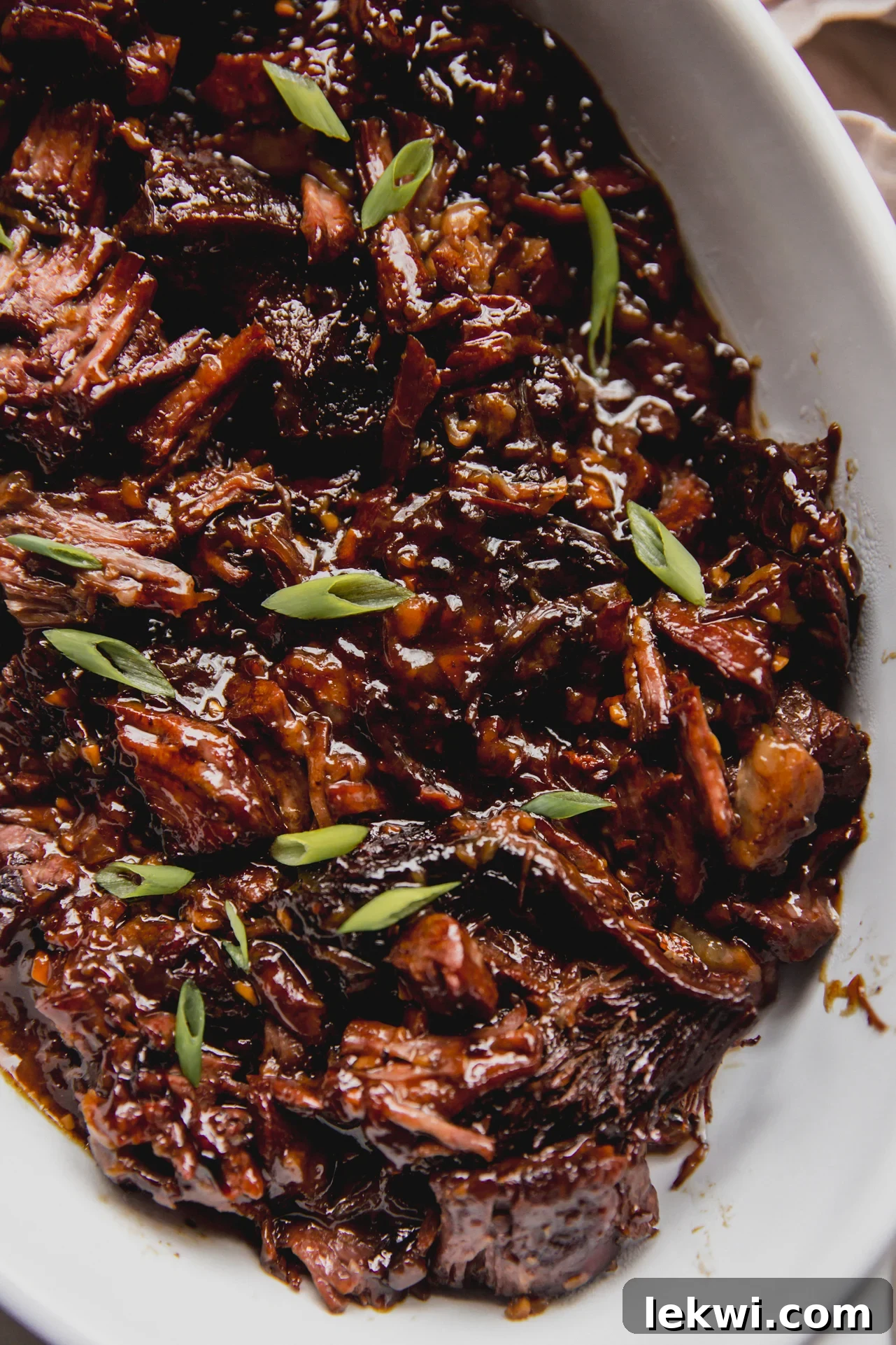 Ginger chuck roast shredded and fully cooked in a large glass dish, topped off with green onion.