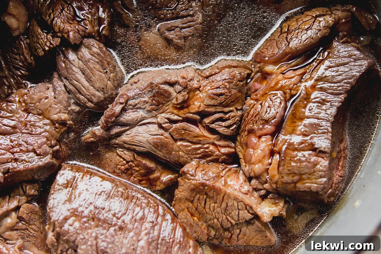 Chuck roast pieces cooked with sliced onion in liquid in a Dutch oven.