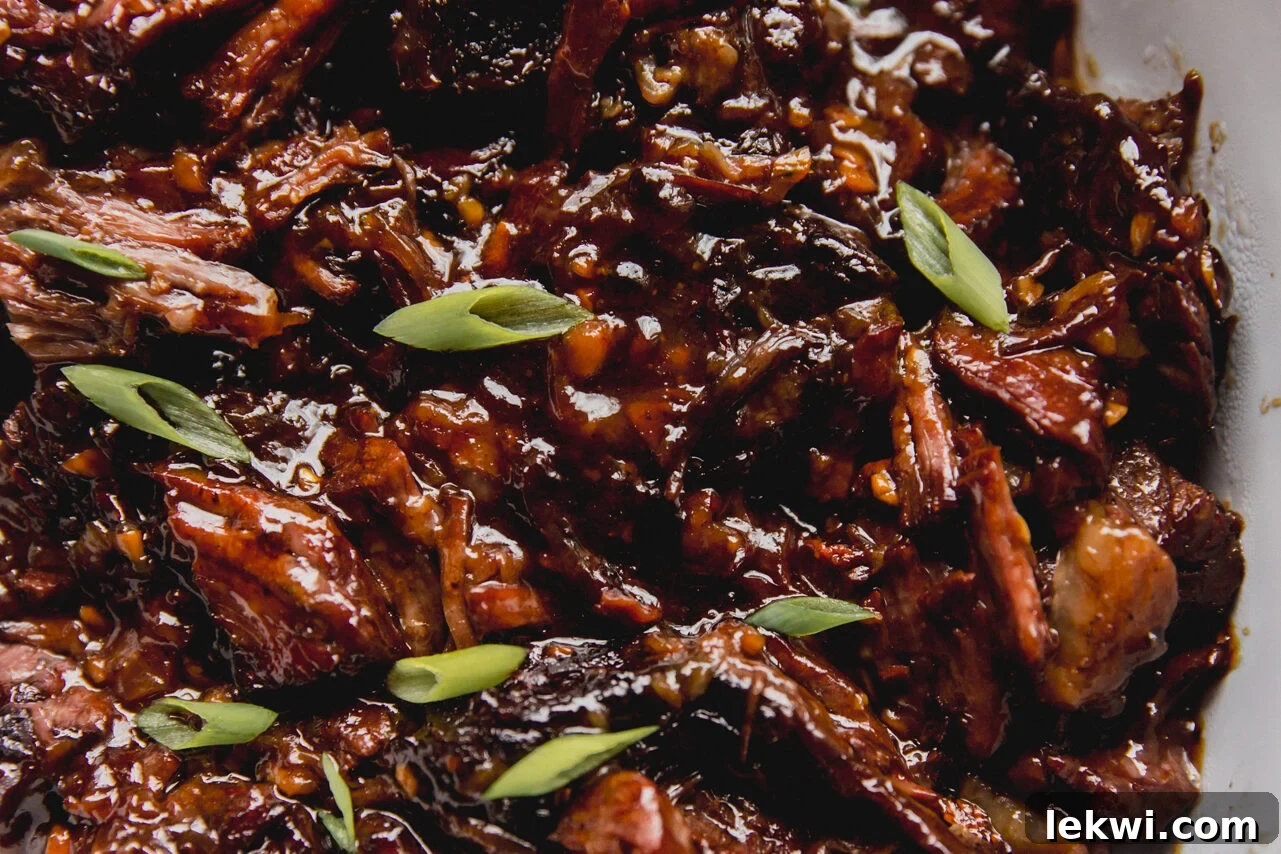 Ginger chuck roast shredded and fully cooked in a large glass dish, topped off with green onion.