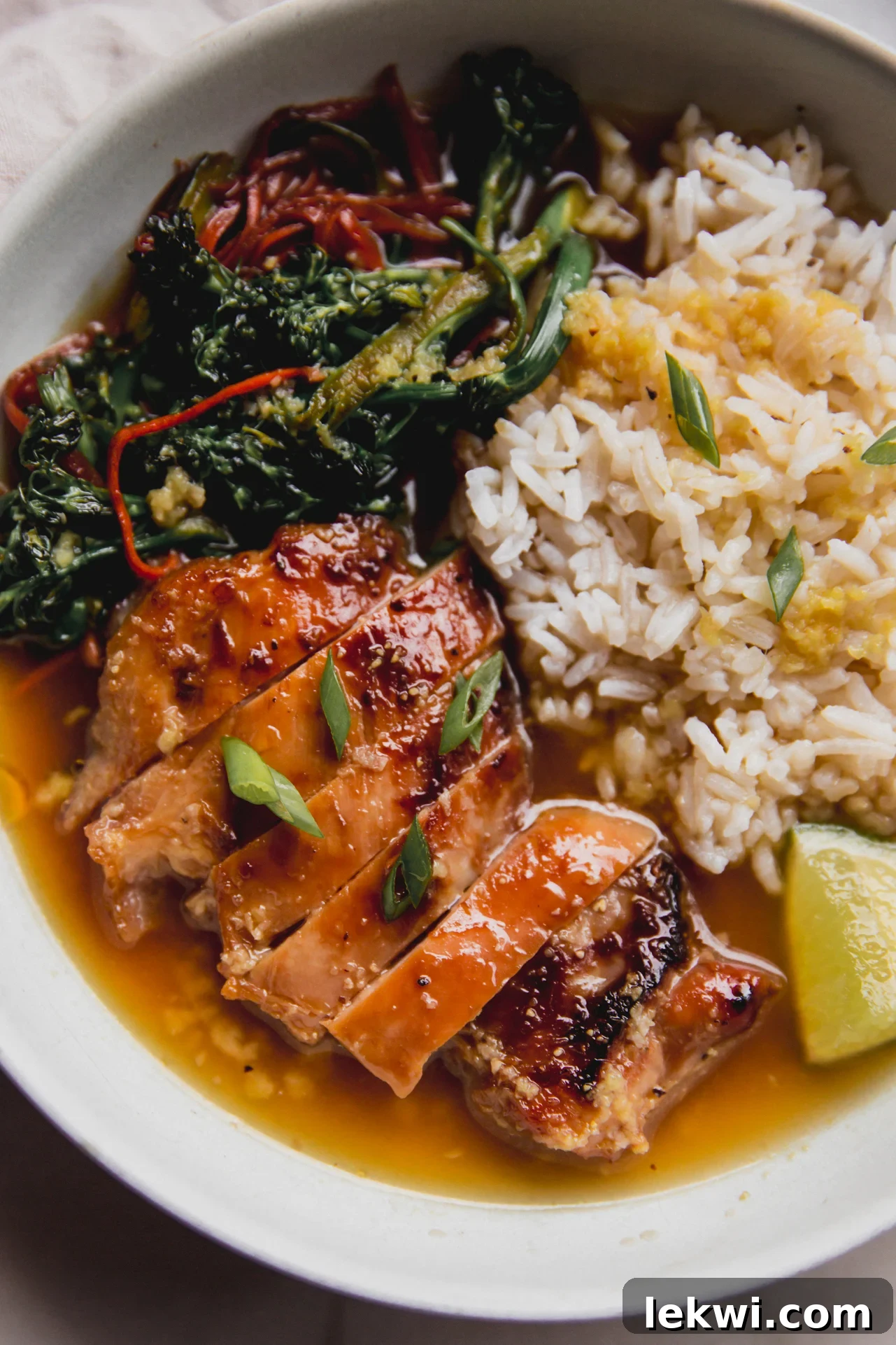 A vibrant bowl of sautéed vegetables, tender sliced chicken thighs, fluffy rice, fresh lime wedges, and fragrant green onion immersed in a golden ginger broth.
